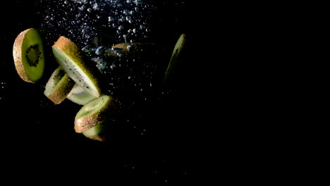 kiwis tombés dans l'eau sur fond noir, côté allumé au ralenti