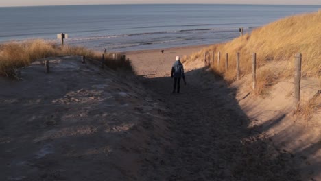 young woman walking down to beach with trash bags on sunny winter day