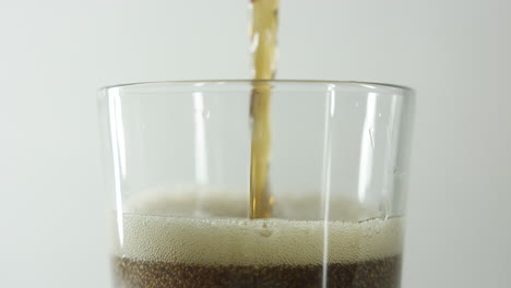 primer plano en cámara lenta de la parte superior de un vaso que se llena con una bebida de cola contra un fondo claro y claro