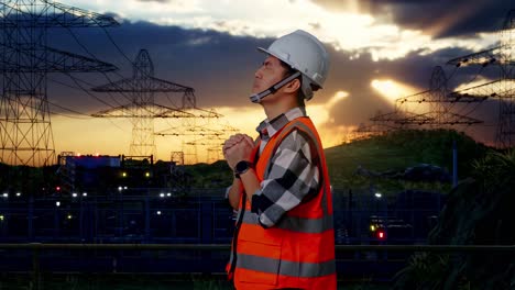 side view of asian male engineer with safety helmet pray for something while standing near high voltage tower