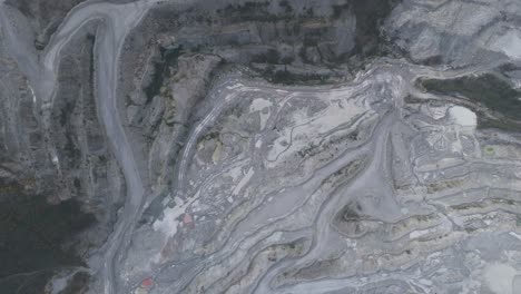 top-down view of active aggregate quarry with spiral haul roads, stepped benches and exposed strata showcasing raw material extraction and industrial geology