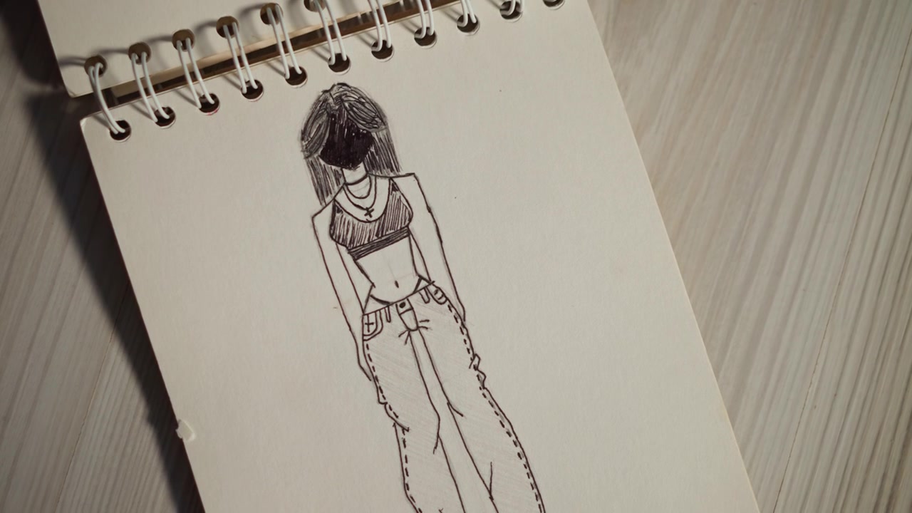 Croquis de silhouette long sur carnet à spirale, dessin de mode en pied avec détails de cheveux texturés, contours à l'encre du pantalon et du torse, fond de parquet de studio, ambiance éditoriale calme, étude de silhouette de modèle.