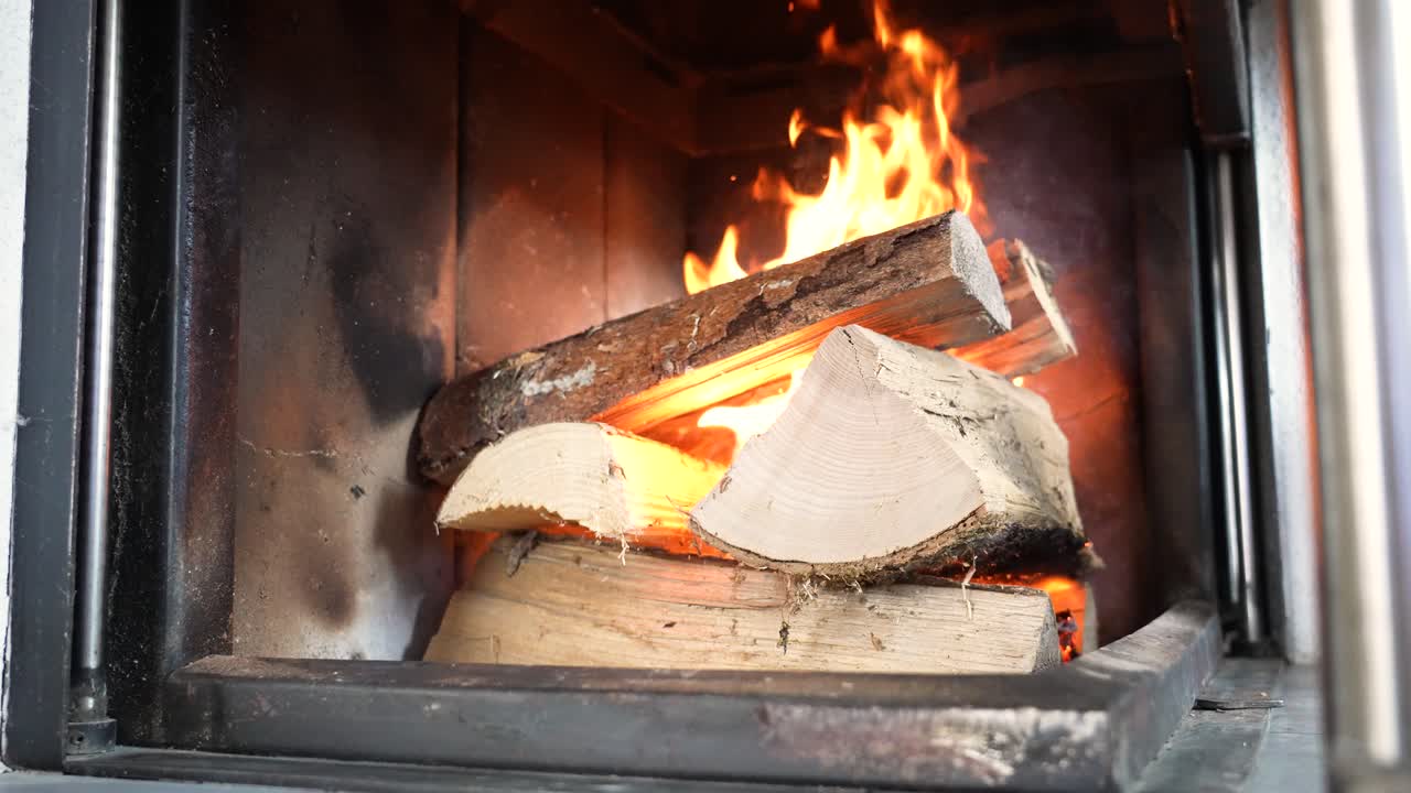 Bliski widok płonącego drewna opałowego w kominku, z jasnymi pomarańczowymi płomieniami. Przytulna scena wnętrza oddająca ciepło, komfort i naturalny ruch ognia w domowej scenerii.
