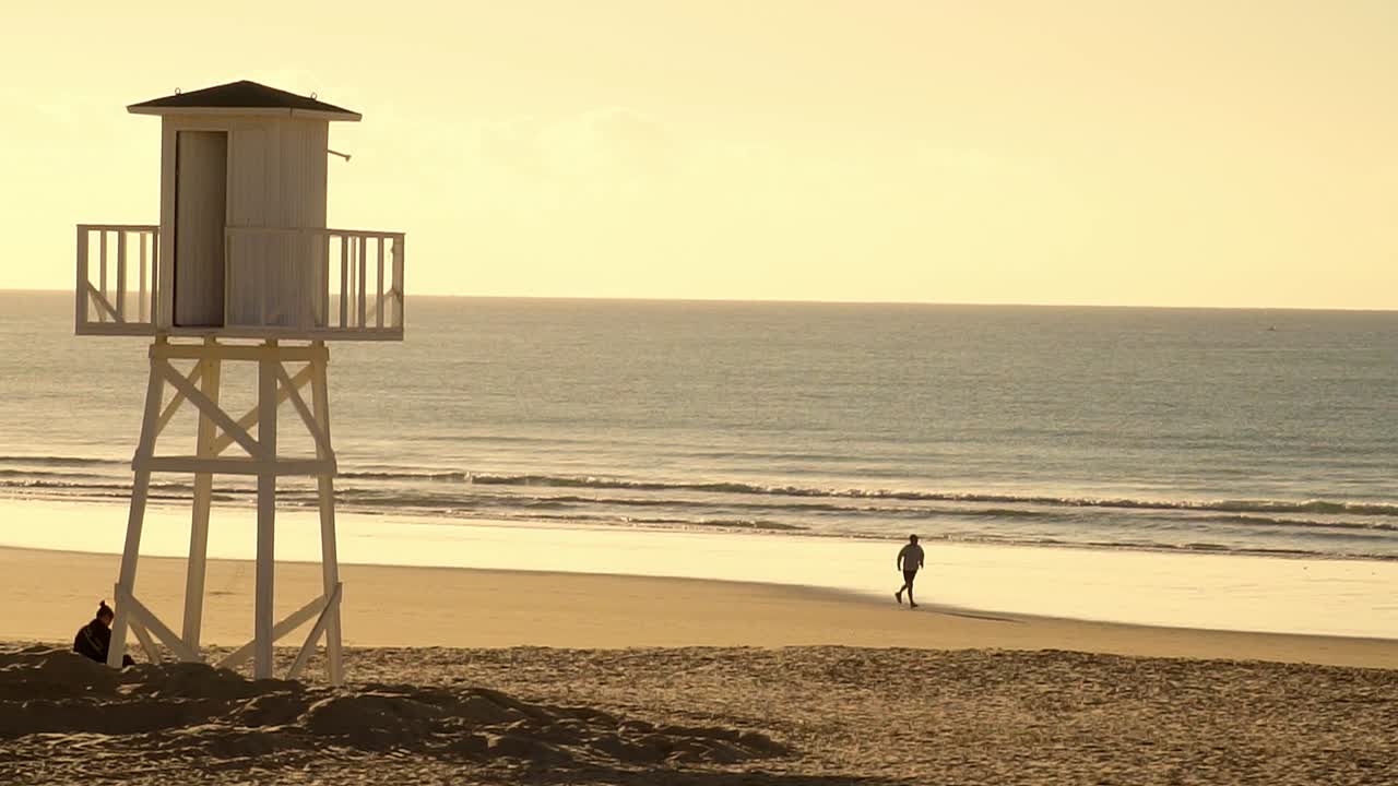 Lifeguard hut on the shore of a beach, and person running in slow motion at sunset
