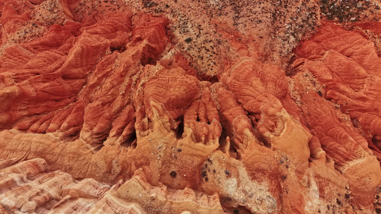 Veduta di formazioni rocciose di canyon che mostrano strati di colori rossi e arancioni con superfici texturizzate sotto una luce diurna intensa.