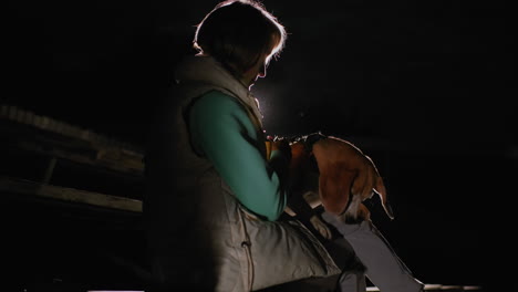 golden retriever climbing trainer's leg during night training session illuminated by soft spotlight creating heartwarming bonding moment between human and dog in peaceful dark outdoor stadium setting