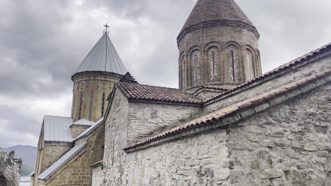 Close-up of the ancient stone architecture and conical domes of the Ananuri Fortress in Georgia. Medieval Orthodox church details against a dramatic cloudy sky in the Caucasus Mountains
