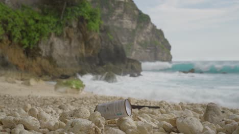 Bote-De-Gas-Desechado-En-La-Playa-Tembeling-De-Guijarros-De-Roca-Con-Olas-En-Segundo-Plano.