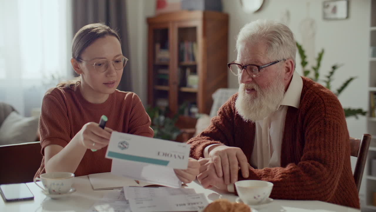 Young Woman Assisting Elderly Grandfather with Household Bills at Home