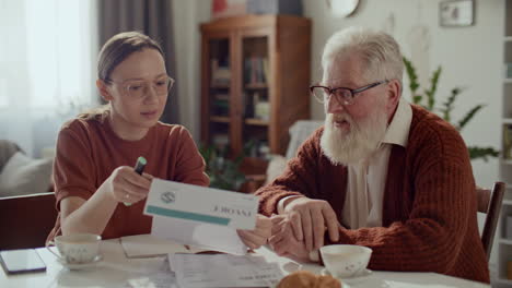 young woman assisting elderly grandfather with household bills at home