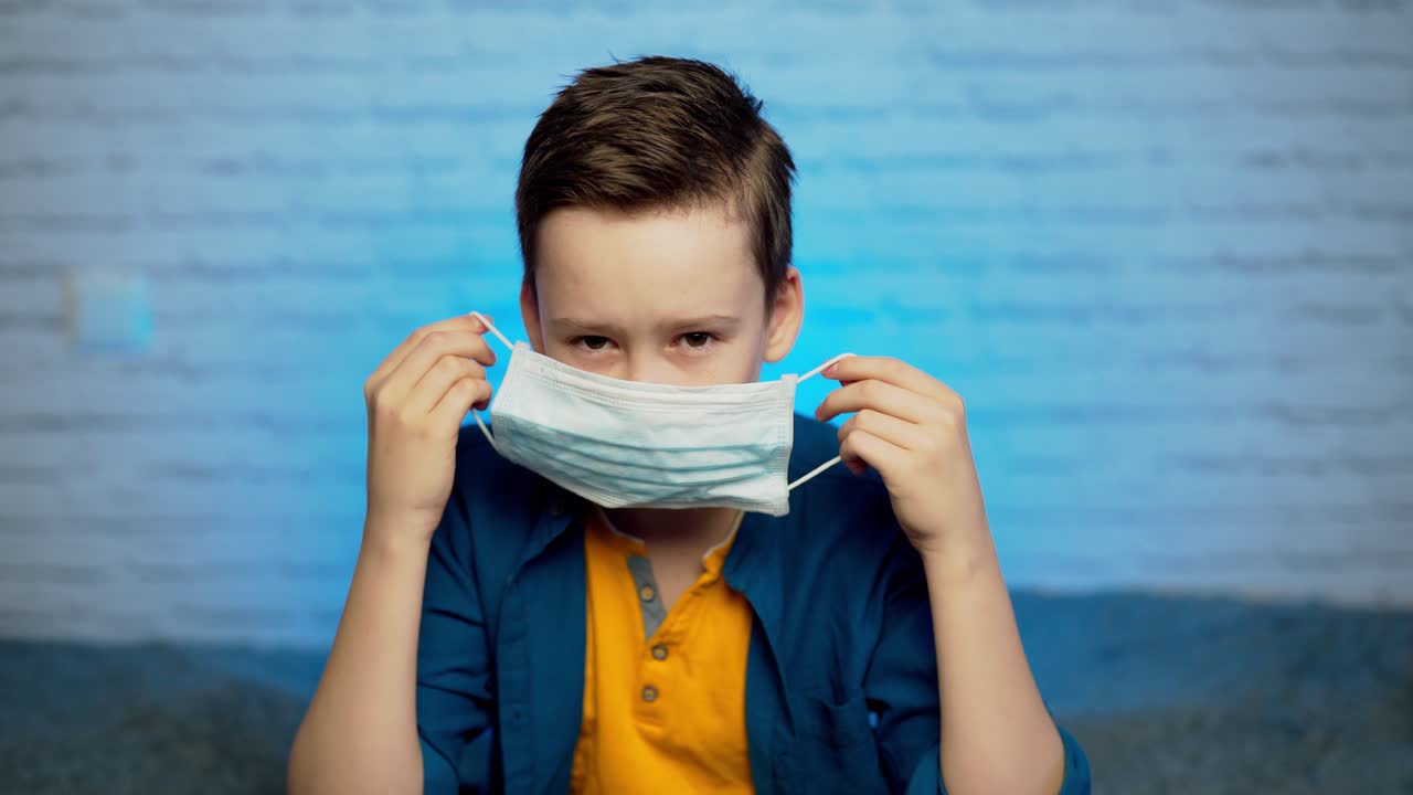 Beautiful boy puts on face medical mask against bacteria and viruses. Pandemic Covid-19. Quarantine in children. Self isolation