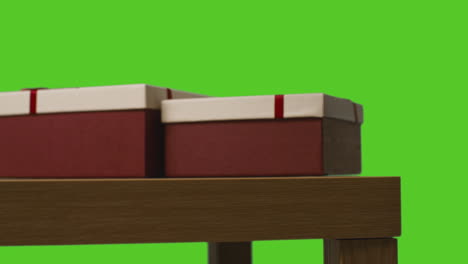 primer plano de un hombre recogiendo y abriendo un regalo envuelto en una mesa contra una pantalla verde