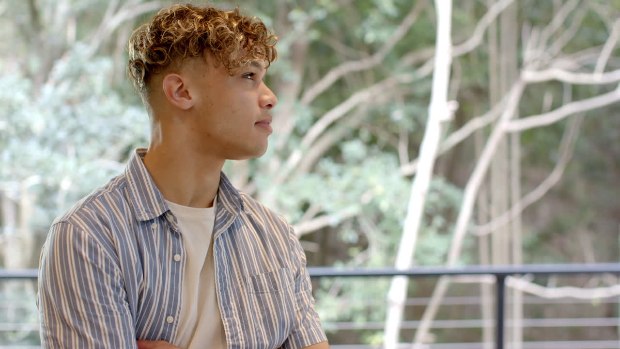 Young man in striped shirt gazing thoughtfully outside, enjoying nature view, copy space