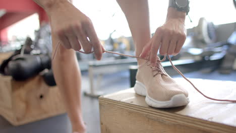 Atleta-Atando-Cordones-En-El-Gimnasio,-Con-Espacio-Para-Copiar