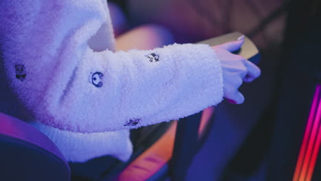close up of hand wearing fluffy sweater grasping and turning adjustment knob on gaming chair rest under neon lighting showcasing tactile interaction and ergonomic detail with vibrant mood