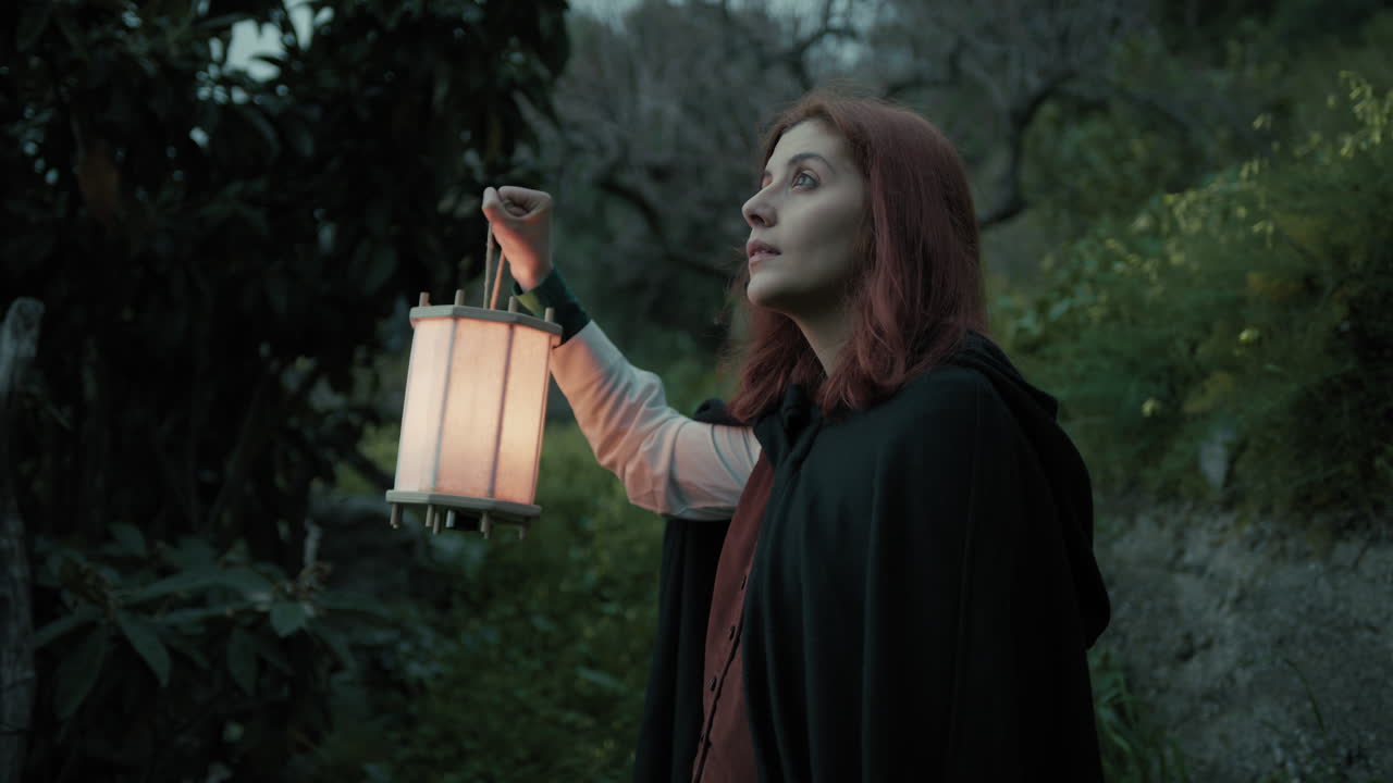 슬픈 여자가 밤에 랜턴과 함께 숲에서 길을 잃고 있습니다.