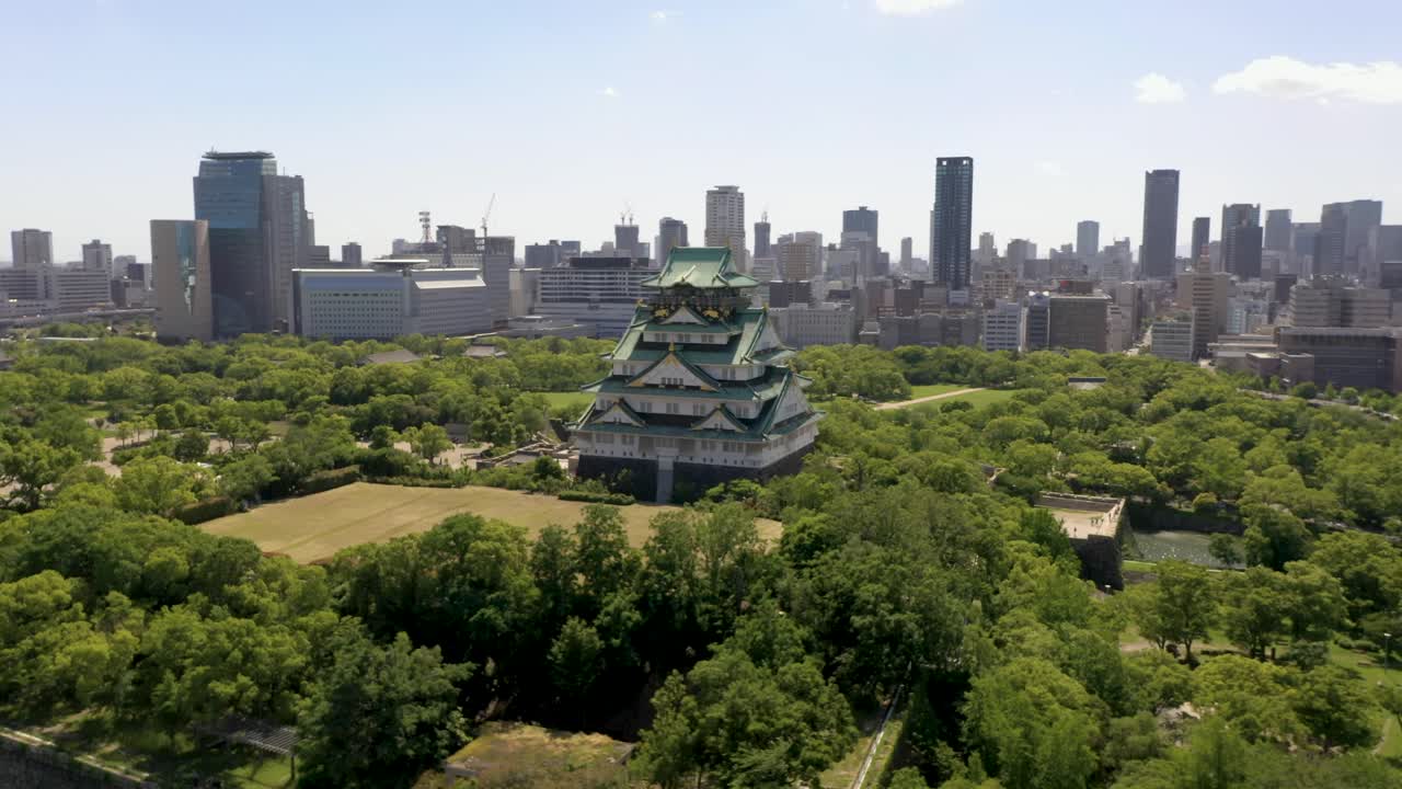 Aerial rising over historic Osaka Castle with park, moat, skyscraper, and city in Osaka, Japan