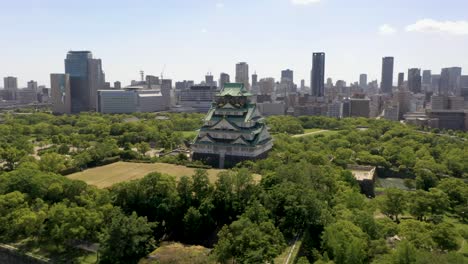 Aerial-rising-over-historic-Osaka-Castle-with-park,-moat,-skyscraper,-and-city-in-Osaka,-Japan