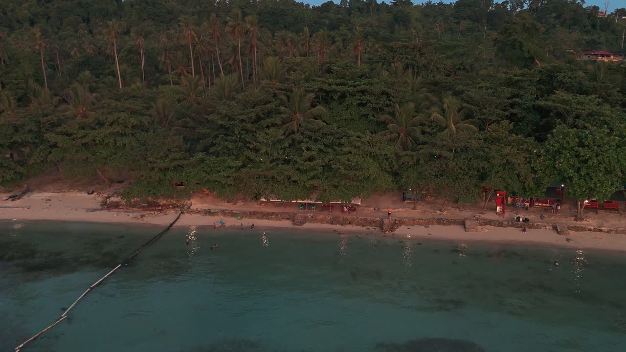 Aerial view of a tropical Philippines beach with palm trees, turquoise waters, and people swimming at sunset. Perfect for travel, tourism, lifestyle, and cinematic projects