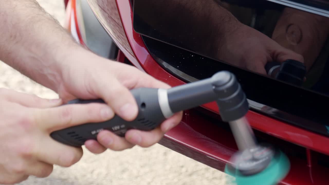 Polishing front bumper lip on dark red car with nano machine polisher and creed pad on extension bar
