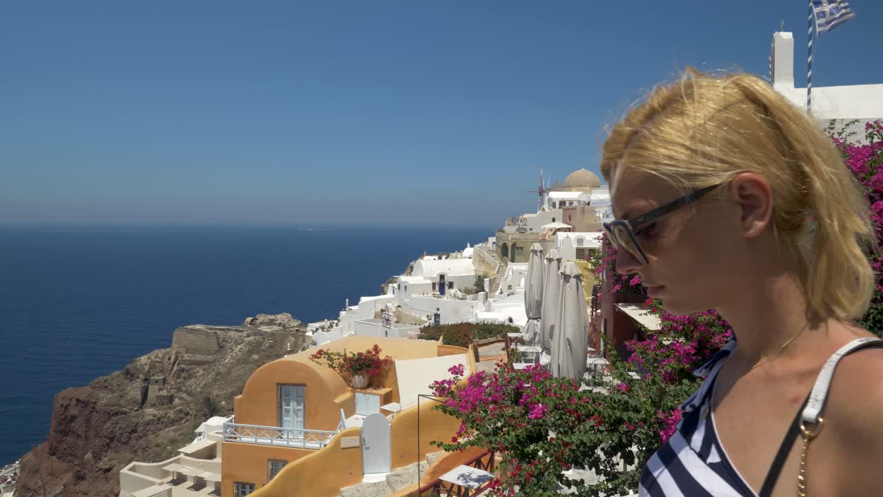 hermosa mujer rubia haciendo turismo en oia, santorini, grecia, tiro lateral