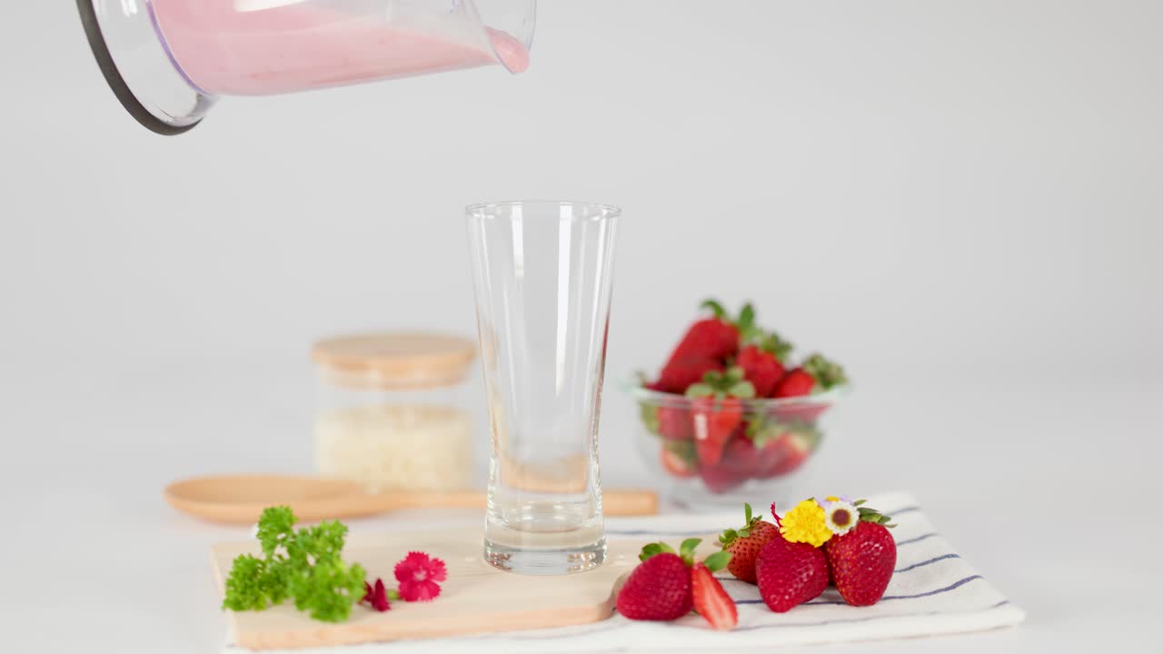 Pink strawberry milkshake poured into tall glass, surrounded by fresh strawberries, bright, soft lighting