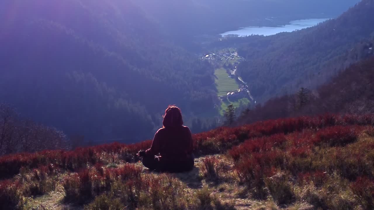 mujer meditando en posición de loto en la cima de una montaña al atardecer relajante vista en órbita sobre el lago con bengala