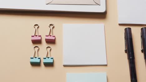 close up of notebook, pens and stationery arranged on beige background, in slow motion