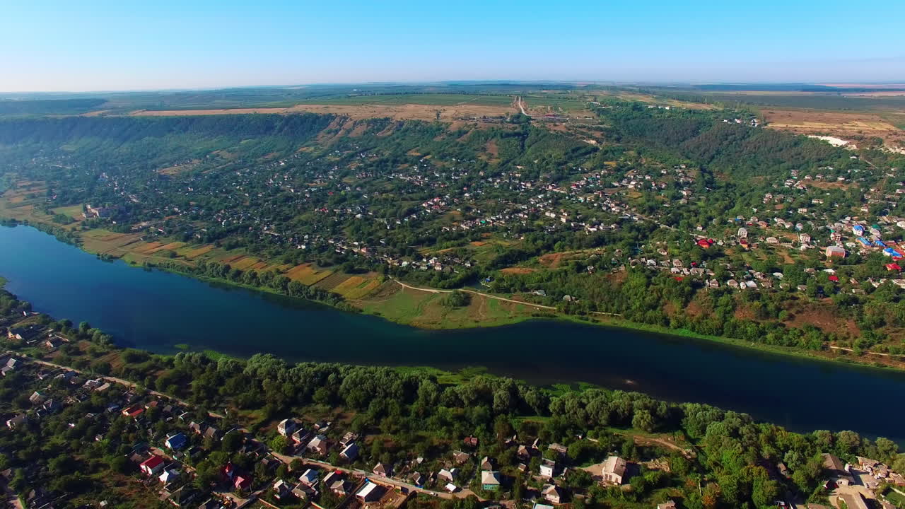 Multiple private cottages in the green city on river banks. Narrow river dividing the city into two parts. Blue sky backdrop. Top view.