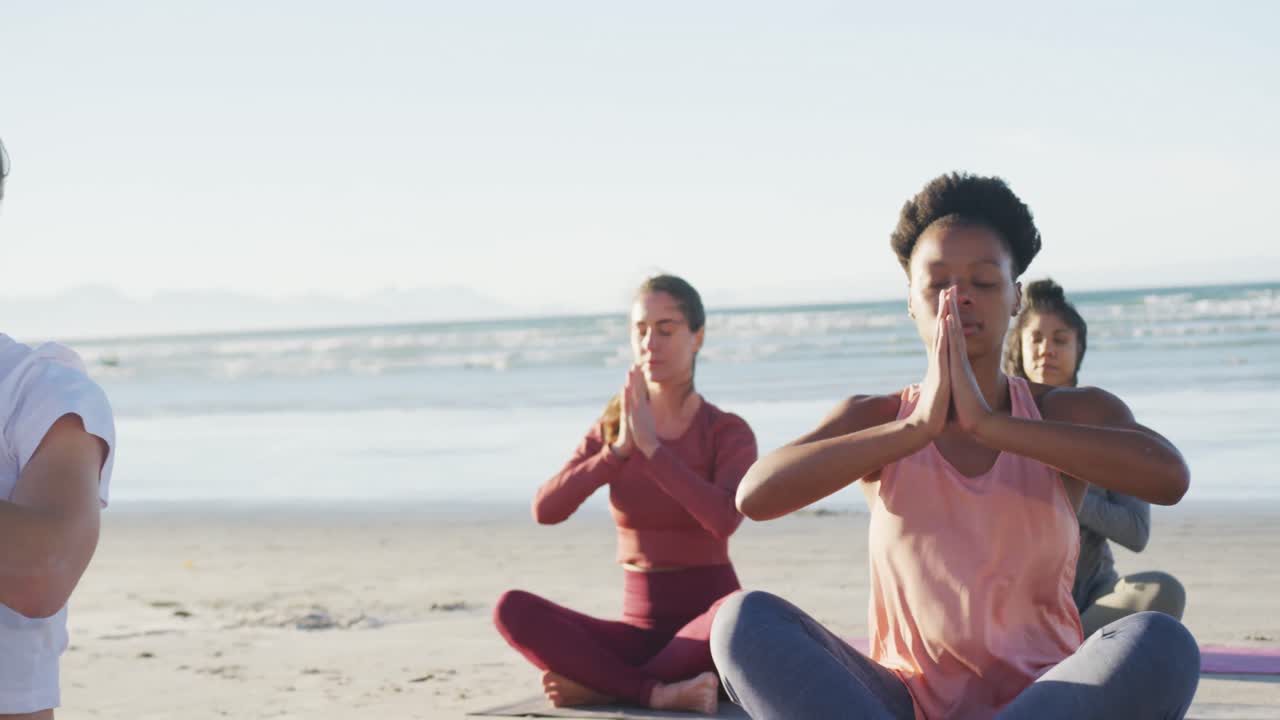 Group of diverse female friends meditating at the beach