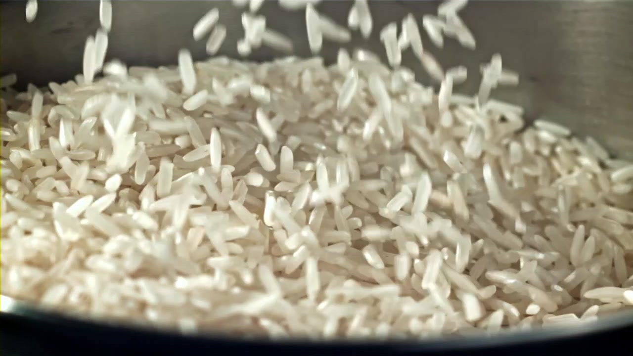 Primo piano al rallentatore di chicchi di riso bianco che cadono in una pentola