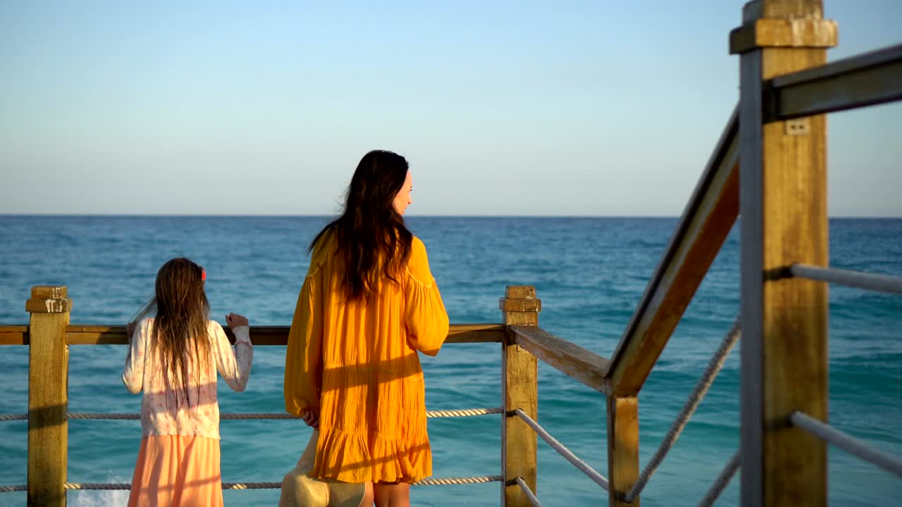 사랑스러운 어린 소녀와 젊은 어머니가 저녁에  해변에서 고 있습니다.