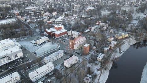 a breathtaking aerial view of valmiera city, showcasing the winding gauja river surrounded by snow-covered landscapes and residential areas under a wintry sky.