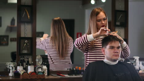 woman barber cuts the hair of a man sitting in a drawer in a men's beauty salon.