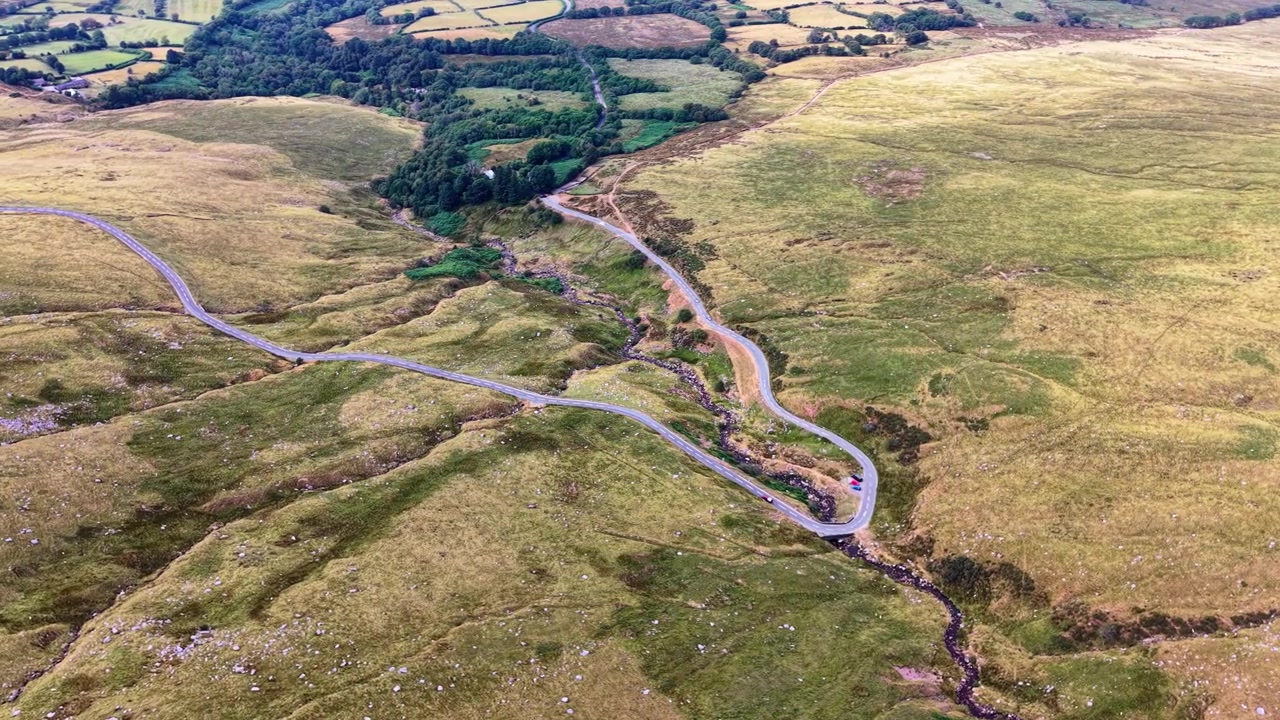Strada rurale che si snoda attraverso il paesaggio dei Brecon Beacons con un piccolo fiume che lo attraversa