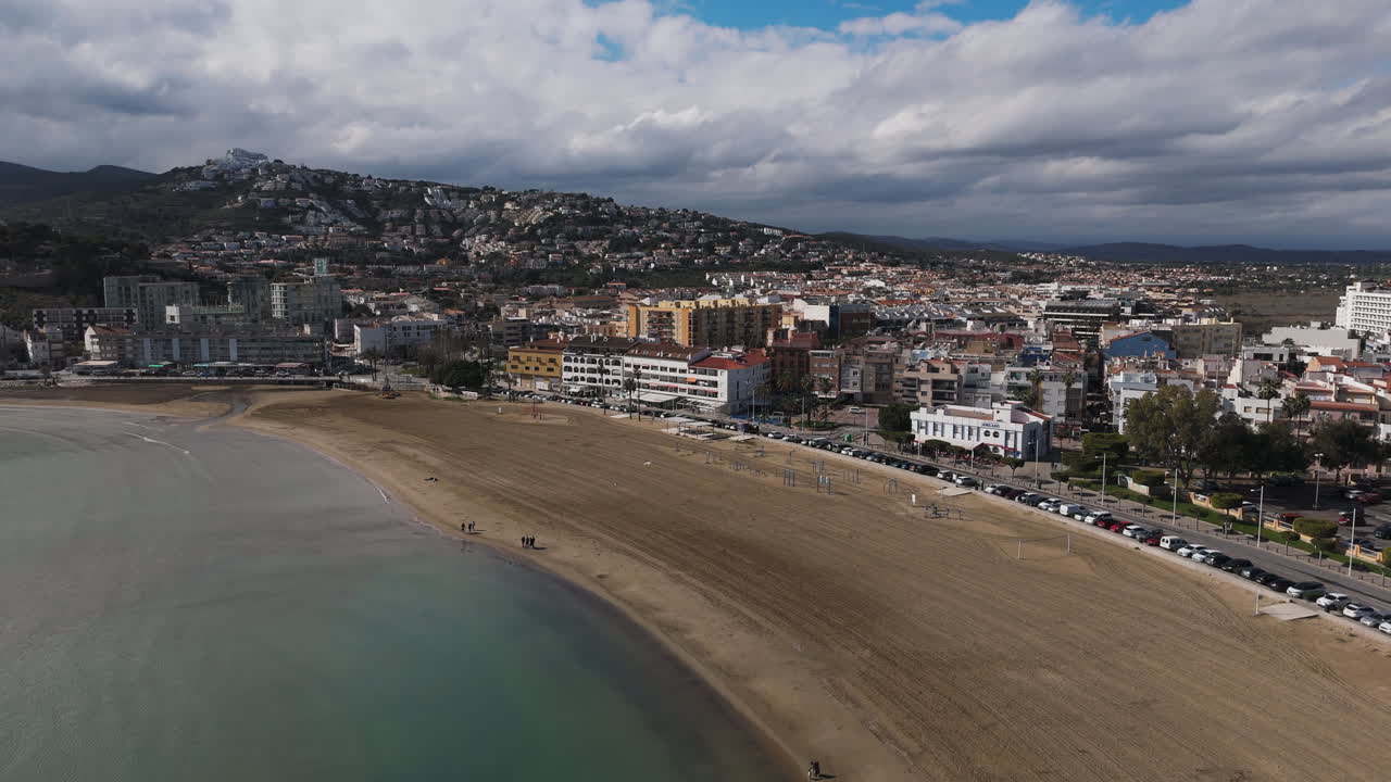 Drone view of Peniscola beach and seafront buildings under cloudy coastal sky