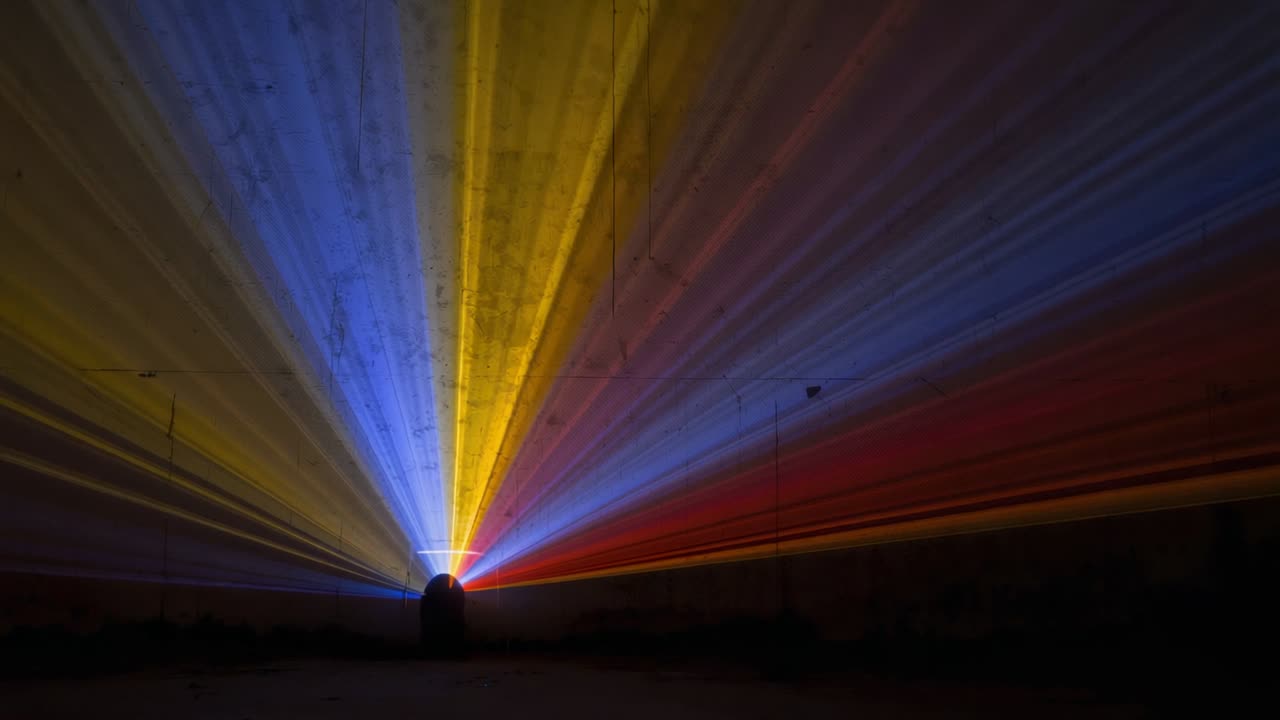 Powering up projector casting red yellow blue beams across dim hangar ceiling with haze