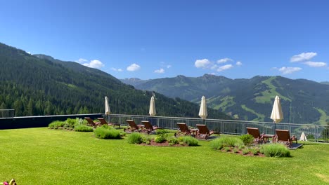 pan shot of luxury garden with tutored lawn in front of gigantic mountain landscape during summer day in austria