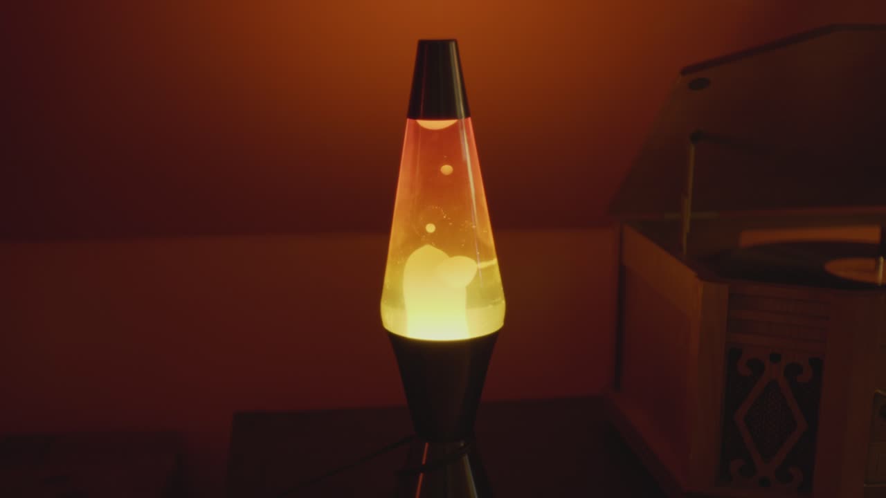 a vintage lava lamp in a warm and retro setting next to a record player. Orange lighting and bubbles create a retro atmosphere. Shot in 60 Frames for slow motion