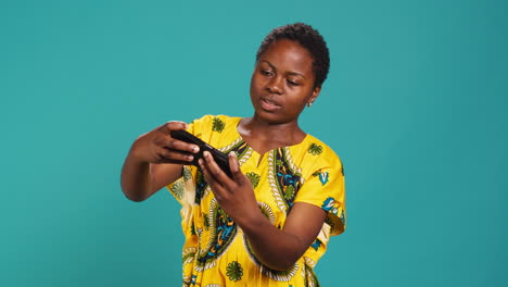 Cheerful-woman-gamer-playing-mobile-videogames-in-studio,