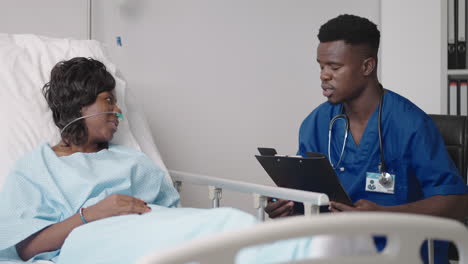 an african male doctor interviews a patient lying in a hospital bed with an oxygen mask. a black woman lying in a hospital bed describes the symptoms to the doctor