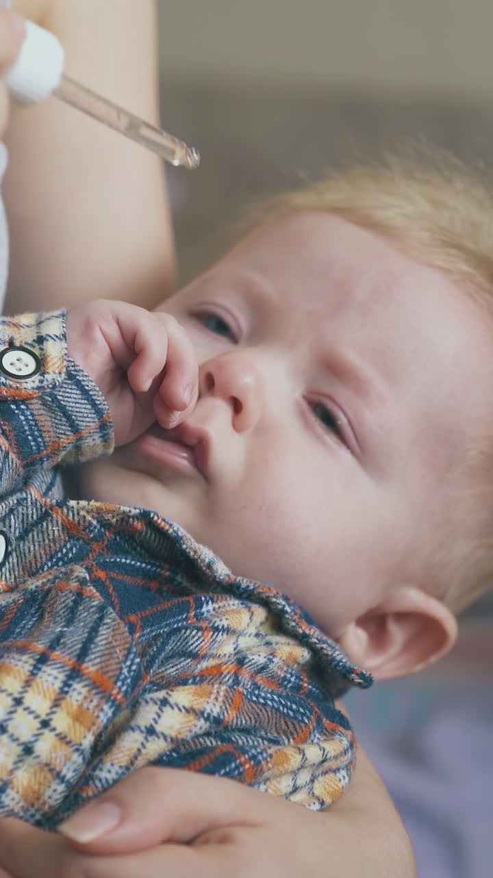 mommy tries to give nasal drops to cute little son holding baby in arms with glass pipette in light room close view