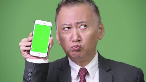 성숙 한 일본인 사업가 가 카메라 에 전화 를 보여주고 있다