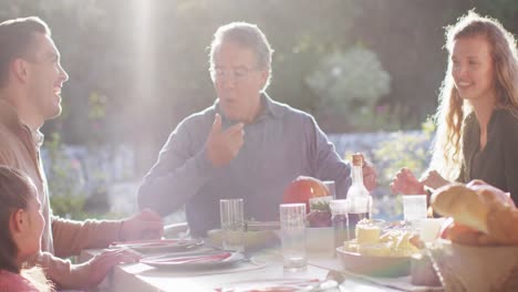 video of happy caucasian parents, daughter and grandparents sitting at sunny outdoor table for meal