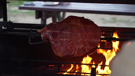 a large piece of pork spinning on a skewer over a fire in a grill box