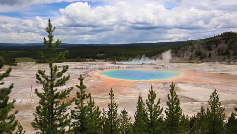 Stunning-panning-view-across-turquoise-geothermal-geyser-Grand-Prismatic-Spring-with-steam-cloud-rising-and-mountains-in-the-background-at-Yellowstone-National-Park,-Wyoming,-USA