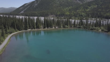 Rising-aerial-reveals-gravel-river-bed-beyond-cold,-clear-mtn-pond