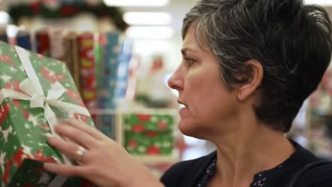 a thoughtful shopper contemplates her choices amidst colorful holiday wrapping papers in a busy store environment