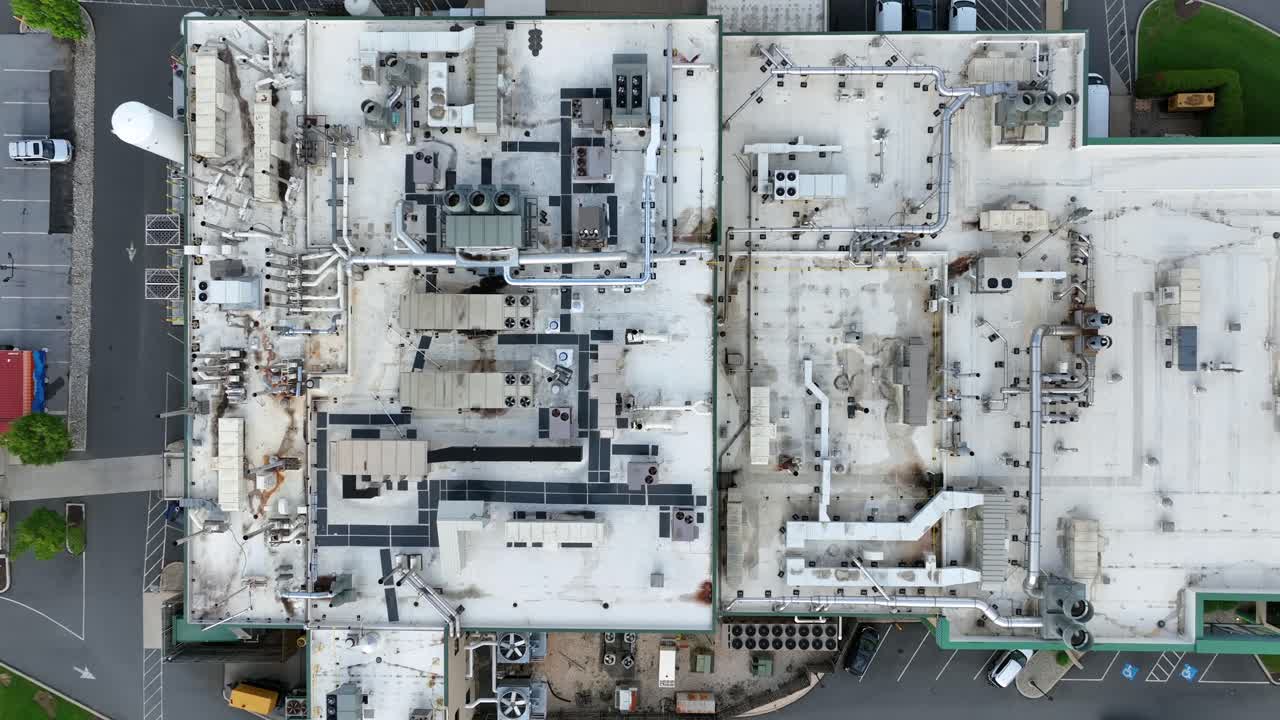Pipelines on roof of factory building with driving cars on street. American industrial area. Parking area and rotating Ventilator. Aerial top down shot.