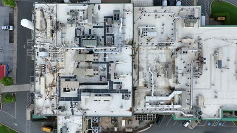 pipelines on roof of factory building with driving cars on street. american industrial area. parking area and rotating ventilator. aerial top down shot.